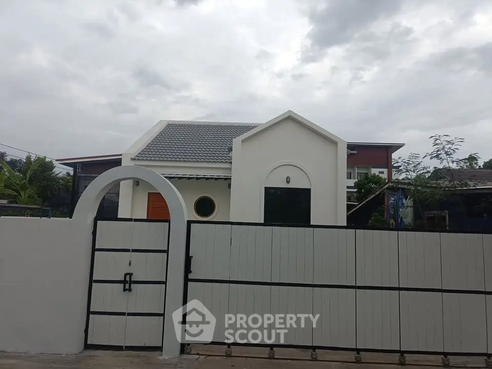 Charming modern house with unique architectural design and gated entrance under cloudy sky.