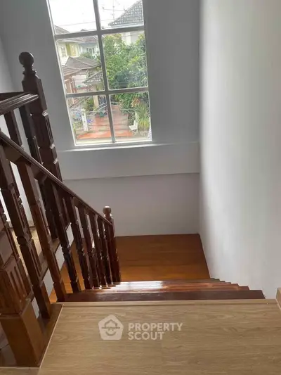 Elegant wooden staircase with large window offering natural light and garden view in a modern home.