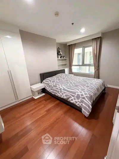 Modern bedroom with wooden flooring and large window in a stylish apartment.