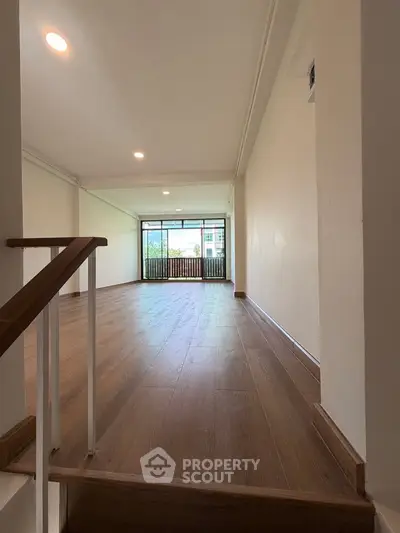 Spacious living room with wooden flooring and large windows offering natural light.