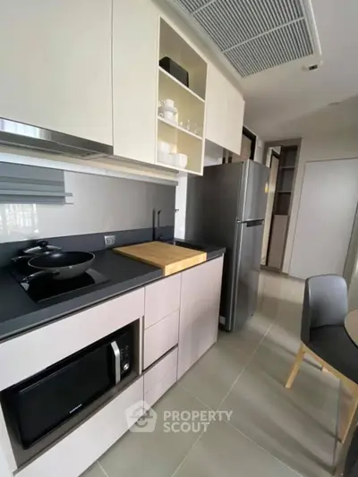 Modern kitchen with sleek cabinetry, built-in microwave, and stainless steel fridge in a compact layout.