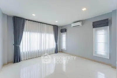 Spacious empty room with large windows and elegant curtains, featuring modern lighting and air conditioning.