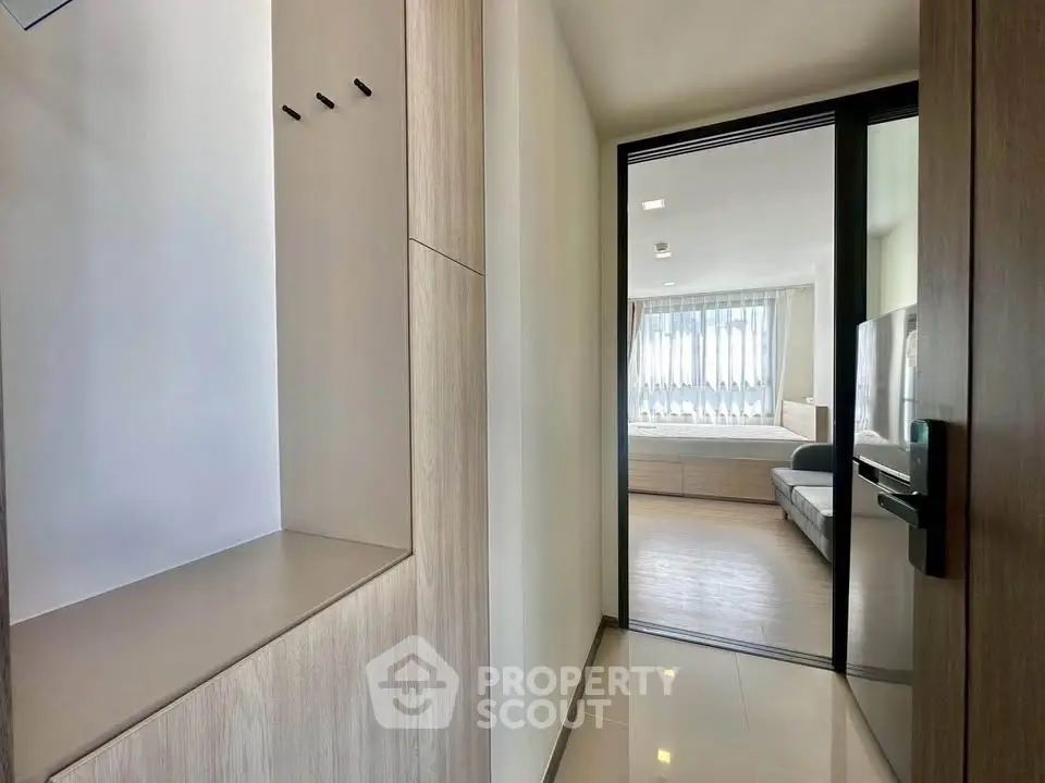 Modern apartment hallway leading to a bright living room with large windows and sleek design.
