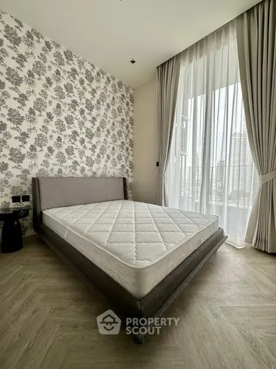 Spacious bedroom with elegant wallpaper and large window offering city views.