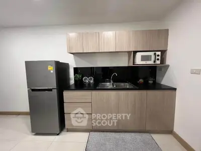 Modern kitchen with sleek cabinetry, stainless steel fridge, and microwave in a stylish apartment.