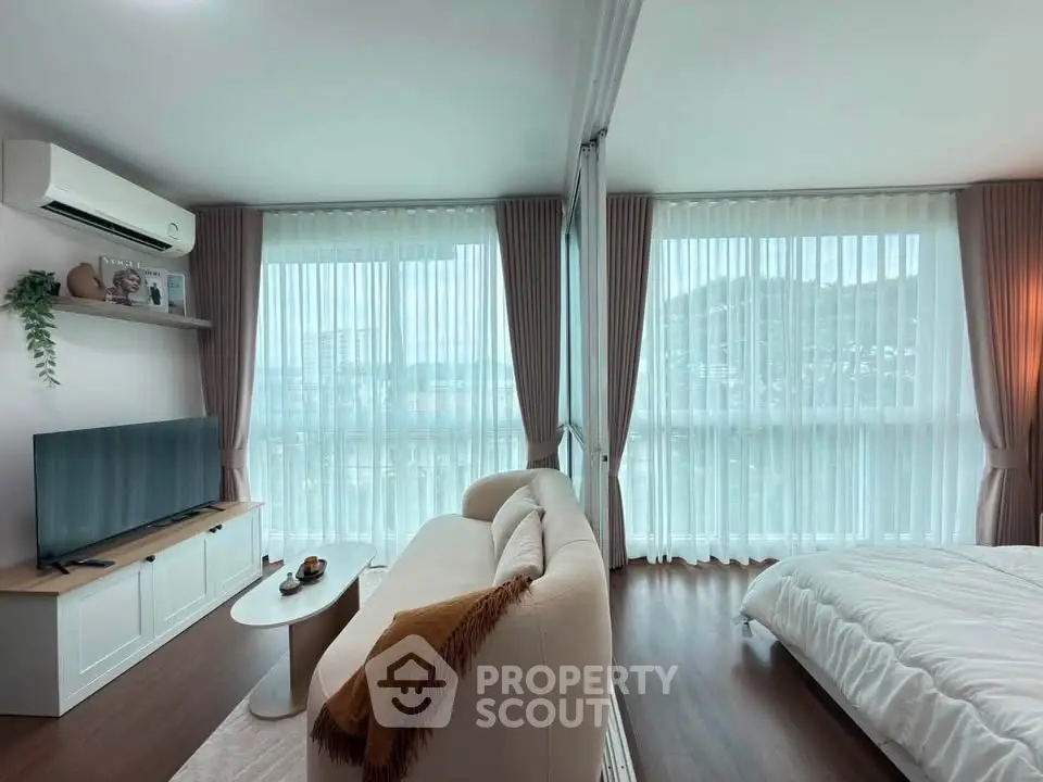Spacious modern living room with large windows and scenic view, featuring cozy sofa and sleek TV setup.