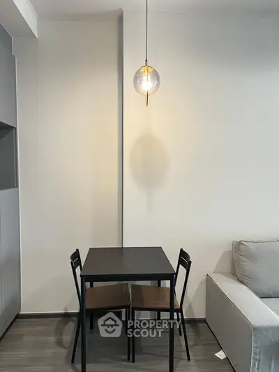 Modern minimalist dining area with sleek black table and chairs, stylish pendant light, and cozy gray sofa.