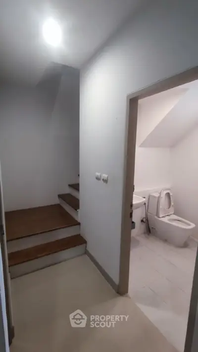 Modern hallway with staircase and bathroom entrance, featuring sleek design and neutral tones.