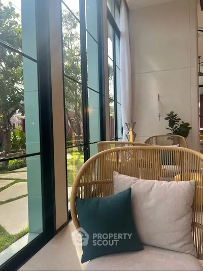 Chic modern living room with large windows and stylish wicker furniture, offering a serene garden view.