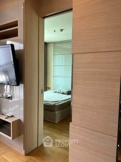 Modern apartment interior with wooden sliding door leading to a cozy bedroom, featuring a wall-mounted TV and sleek design.