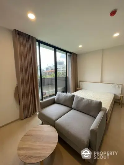 Compact and modern studio apartment with a comfortable bed, cozy sofa, and ample natural light from the large window, perfect for urban living.