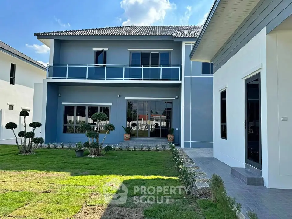 Modern two-story house with manicured lawn and spacious balcony, showcasing elegant architecture.