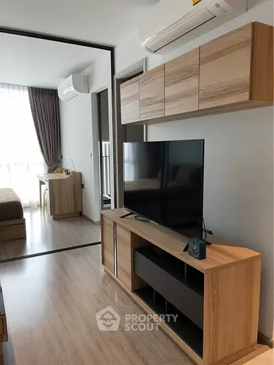 Modern living room with sleek wooden furniture and large TV, adjacent to a cozy bedroom.