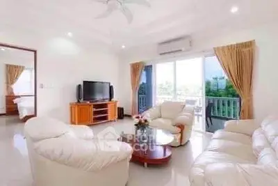 Spacious living room with elegant white sofas and large windows offering natural light and garden view.