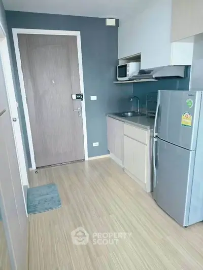 Modern compact kitchen with sleek appliances and wooden flooring in a cozy apartment.