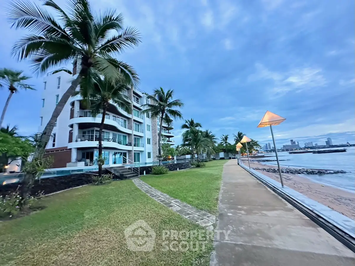 Luxurious beachfront apartment building with palm trees and ocean view at sunset.