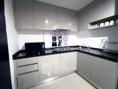 Modern kitchen with sleek cabinetry and black countertops, featuring a microwave and stylish backsplash.