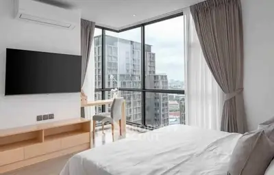 Modern bedroom with large windows offering stunning city views, featuring a sleek TV and cozy workspace.