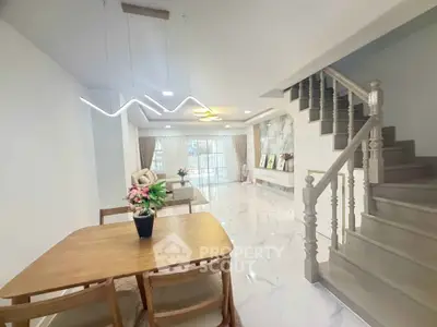 Spacious modern living room with elegant staircase and dining area, featuring stylish lighting and open layout.