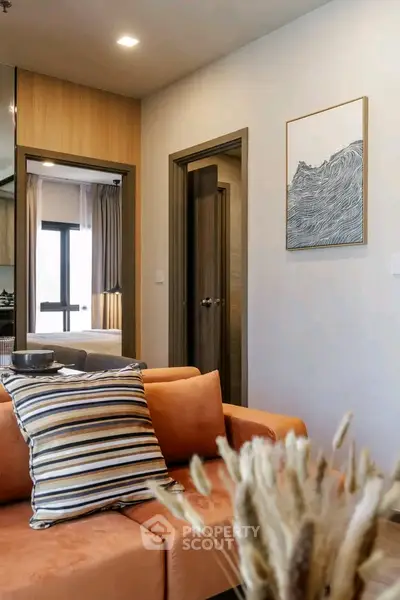 Modern living room with stylish decor and cozy orange sofa, showcasing a glimpse into a bedroom.