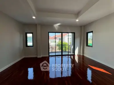 Spacious living room with polished wooden floors and large windows offering natural light and a balcony view.