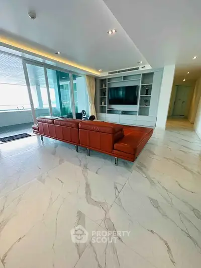 Spacious modern living room with leather sofa and large TV, featuring marble flooring and balcony access.