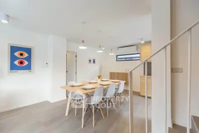 Modern dining area with stylish wooden table and chairs, open layout to kitchen, bright and airy ambiance.