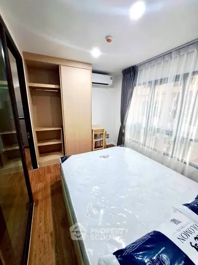 Modern bedroom with large window, wooden flooring, and built-in wardrobe in a stylish apartment.