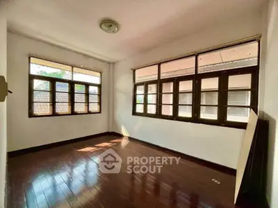 Spacious sunlit room with wooden flooring and large windows, perfect for a cozy living space.