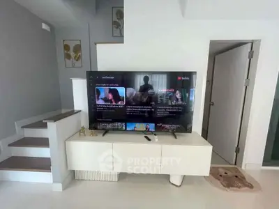 Modern living room with sleek TV setup and stylish staircase, perfect for contemporary living.