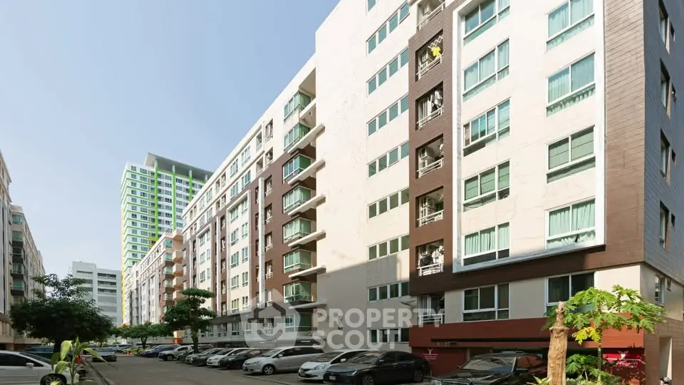 Modern apartment building exterior with parking area and lush greenery.