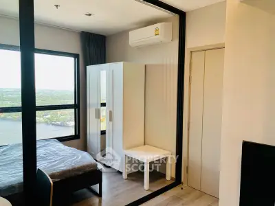Modern bedroom with large window offering stunning river view, featuring sleek furniture and air conditioning.