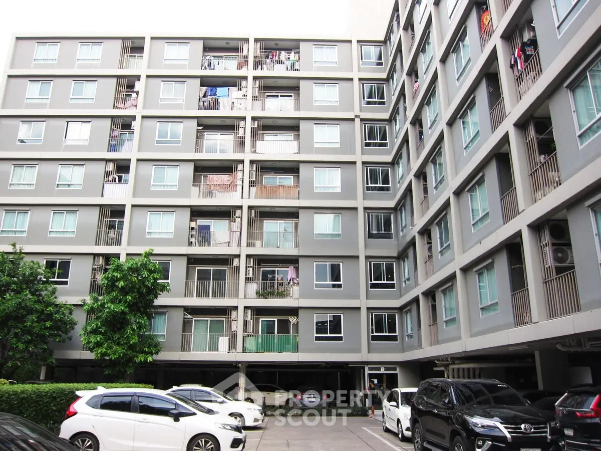 Modern apartment building exterior with parking area and multiple balconies.