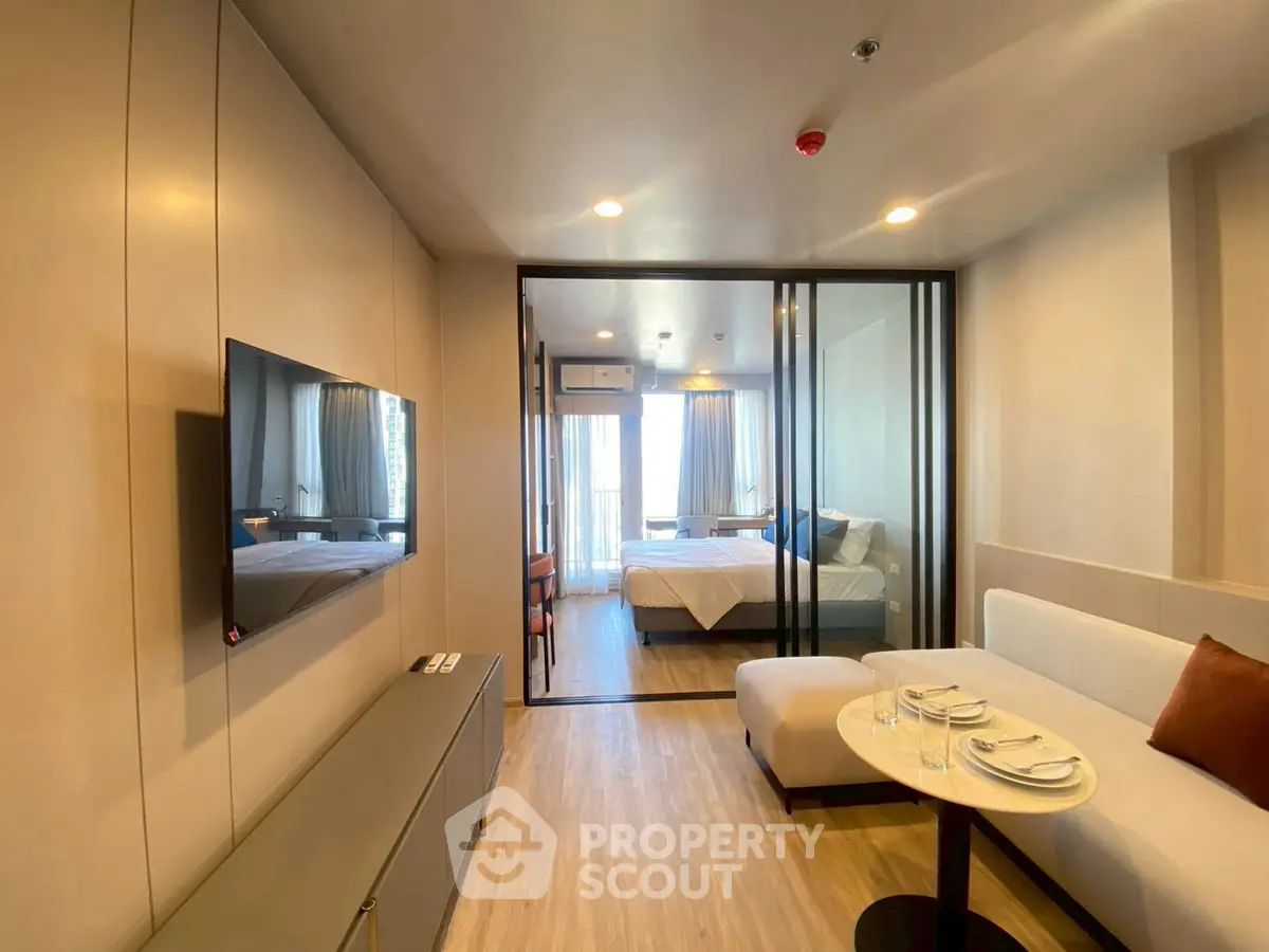 Modern apartment interior with open living room and bedroom, featuring sleek design and natural light.