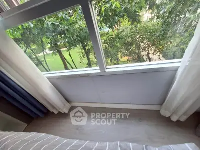 Cozy bedroom with large window offering lush garden view, perfect for nature lovers.