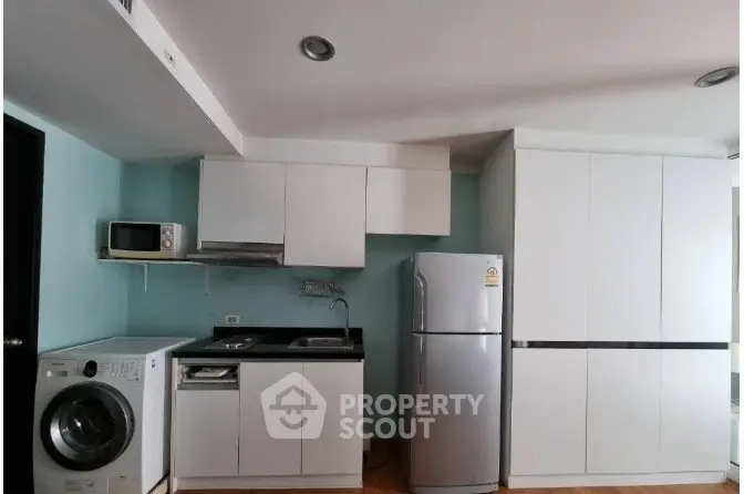Modern kitchen with sleek white cabinets, stainless steel fridge, and washing machine in compact layout.