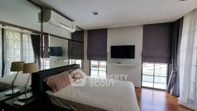 Modern bedroom with large windows and wall-mounted TV, featuring elegant decor and natural light.