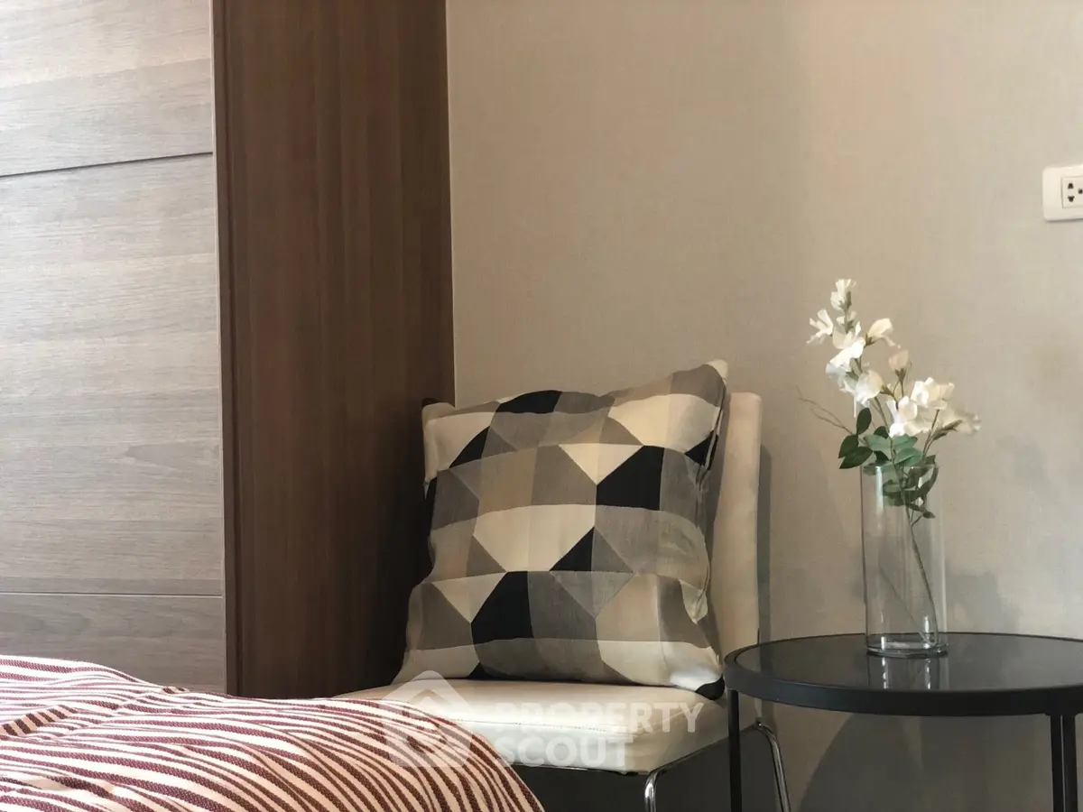 Cozy bedroom corner with modern chair, geometric cushion, and elegant floral decor.