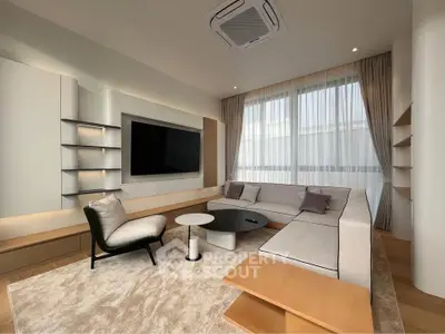 Modern living room with sleek furniture and large TV, featuring elegant decor and ample natural light.