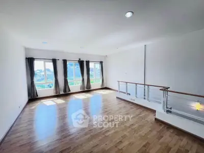 Spacious sunlit living room with wooden flooring and large windows offering a scenic view.