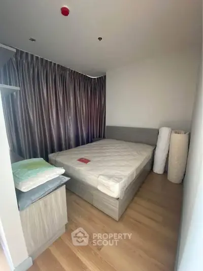 Cozy bedroom with wooden flooring and modern furnishings, featuring a large window with elegant curtains.