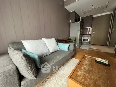 Modern living room with cozy gray sofa, wooden coffee table, and compact kitchen area in open layout apartment.