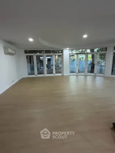 Spacious living room with large windows and wooden flooring, perfect for natural light and modern living.