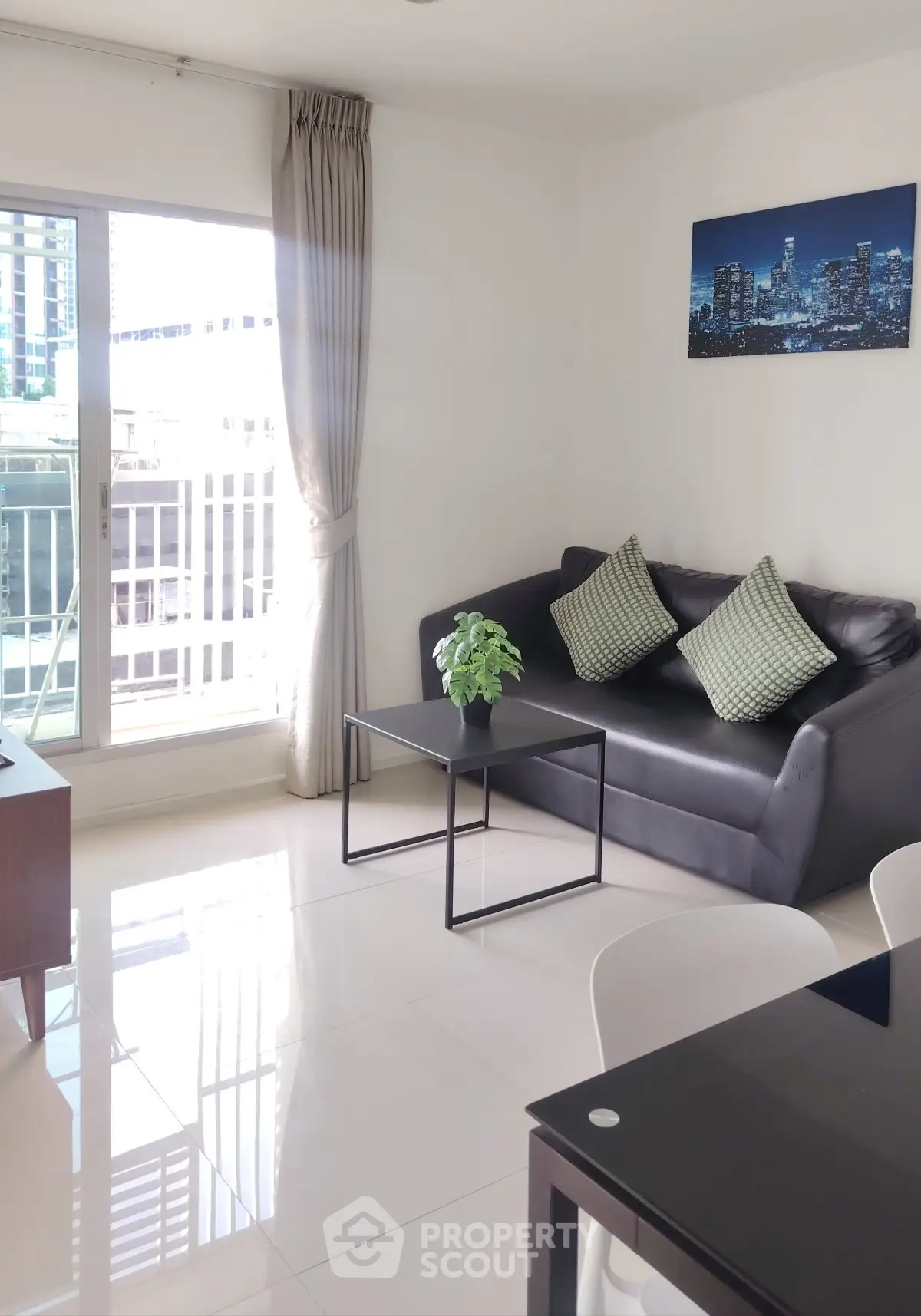 Modern living room with sleek black sofa, cityscape artwork, and large window offering natural light.
