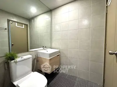 Modern bathroom with sleek fixtures and neutral tiles, featuring a compact vanity and toilet.