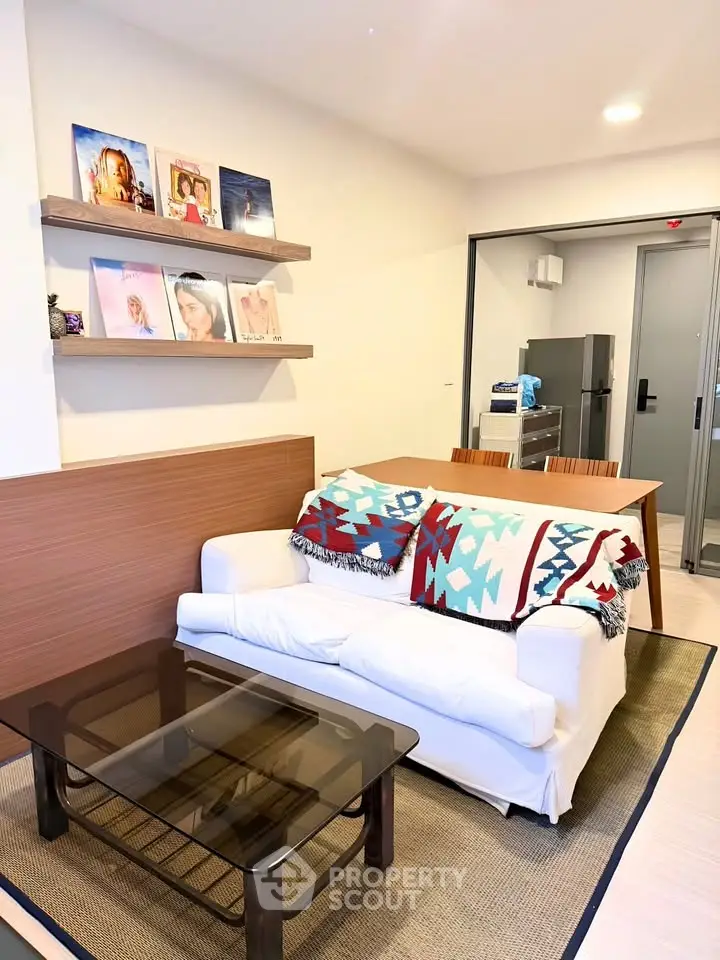 Modern living room with stylish decor and open kitchen layout, featuring cozy seating and contemporary shelving.