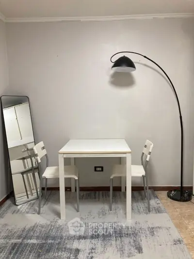Minimalist dining area with white table, chairs, and floor lamp in modern apartment.