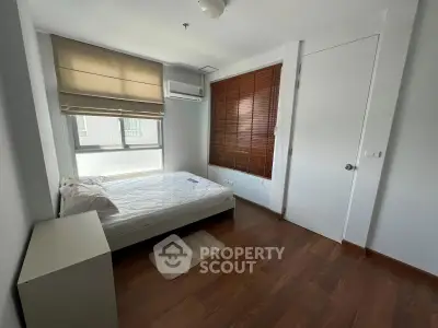 Cozy bedroom with wooden flooring and ample natural light, featuring a comfortable bed and modern window blinds.