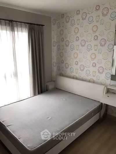 Cozy bedroom with unique clock-themed wallpaper and natural light from large window.