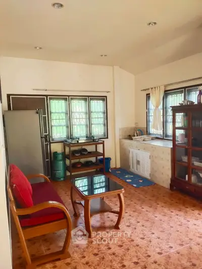 Cozy living room with natural light, featuring a wooden sofa, glass coffee table, and a compact kitchen area.